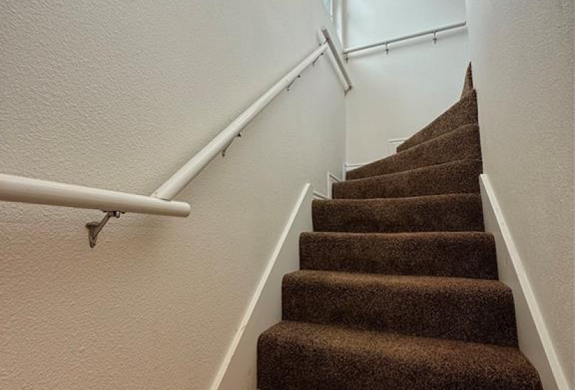 Carpeted staircase with inviting wall sconces and natural light from small windows.  There is a pocket door feature at top of stairs offering additional privacy to bedroom.