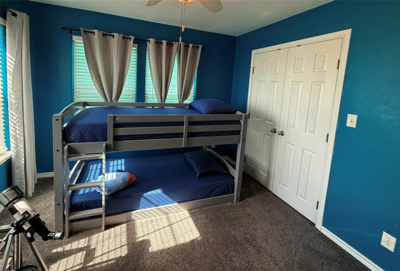 Bunk room with vibrant blue walls. It has a carpeted floor and a closet with double doors.