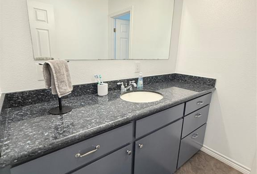 Bright bathroom with a large mirror and modern lighting in main part of house. Features a dark granite countertop with private door to tub and toilet.