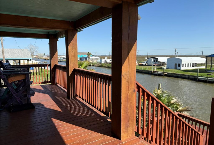 Covered deck with wooden railing overlooking canal, ideal for relaxing and enjoying the sunrise over the water.
