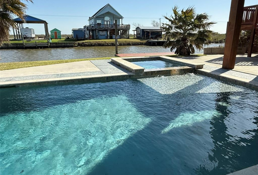 This photo showcases a beautiful outdoor heated pool with a hot tub, set against the backdrop of a serene canal.