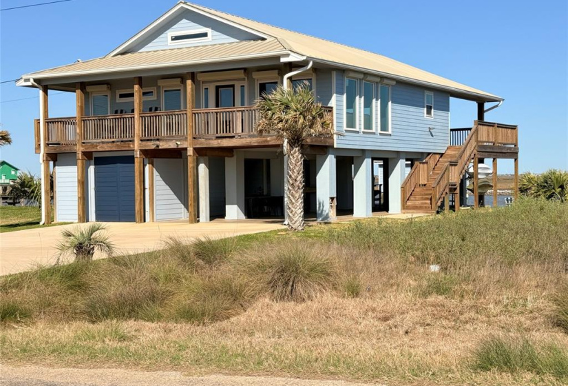 This elevated coastal home features a spacious wooden decks, light blue siding, and a metal roof. It offers ample outdoor space with a covered area below and an external staircase. Ideal for enjoying beachside living.