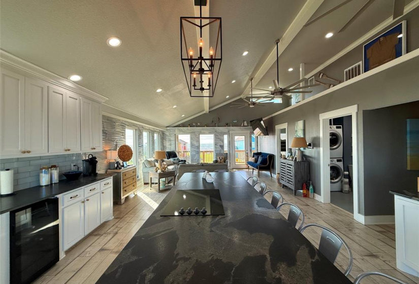 Modern kitchen with stainless steel appliances, white cabinetry, and sleek black countertops. It features a double-door fridge, wine cooler, built-in oven and microwave. The space is bright with plenty of natural light and recessed lighting.