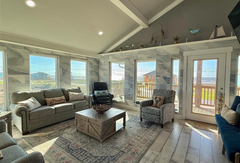 This bright, inviting living room features vaulted ceilings, large windows offering ocean views, and stylish decor with a beach theme.