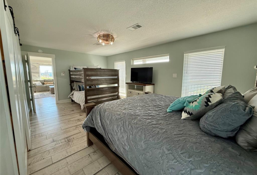 This bedroom features soft blue walls and wood flooring, with a ceiling fan for comfort. It includes a bed with decorative pillows and a nightstand with a lamp, offering a welcoming and relaxing atmosphere.