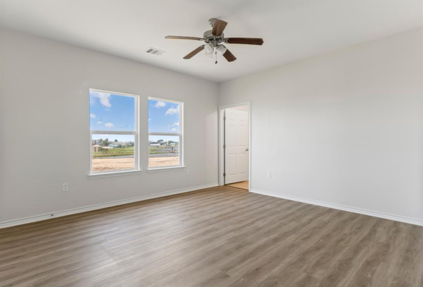 Expansive primary bedroom boasts two walk in closets. A glimpse of the beautiful en-suite bath, Note the soaring ceilings, wood look LVP flooring and neutral paint.