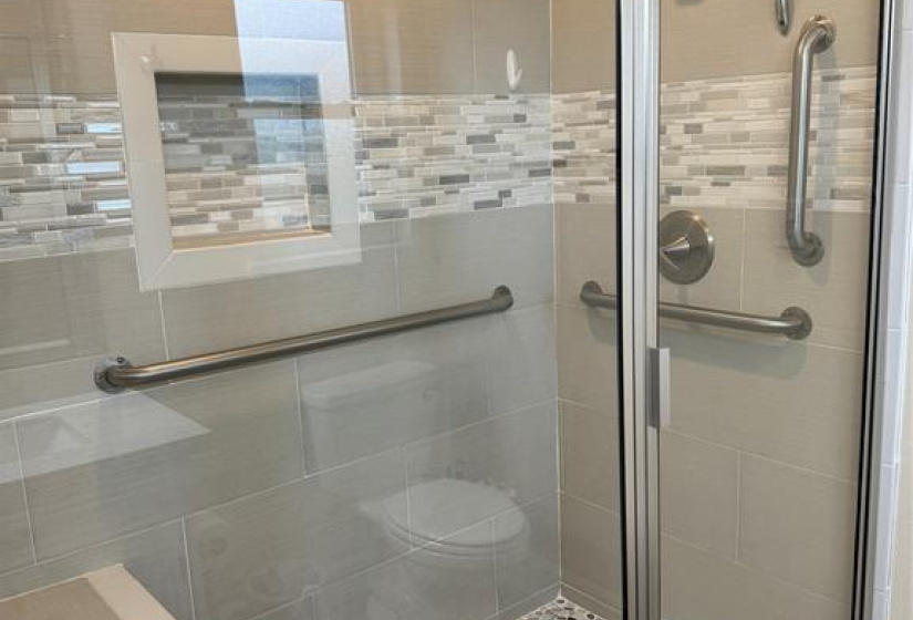 Very large, custom shower with a big bench and bars for accessibility. Lots of glass makes this shower light and bright!